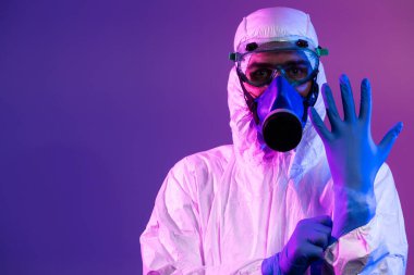 Coronavirus covid-19 salgını. Küresel sağlık salgını uyarısı ve mavi ve pembe neon ışıklı arka plandaki tehlike nedeniyle koruyucu biyolojik kıyafet ve maske giyen doktor.