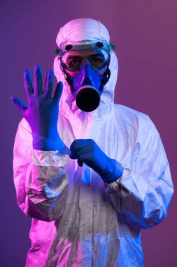 Coronavirus covid-19 salgını. Küresel sağlık salgını uyarısı ve mavi ve pembe neon ışıklı arka plandaki tehlike nedeniyle koruyucu biyolojik kıyafet ve maske giyen doktor.
