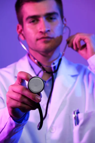 白衣英雄的画像 带着听诊器的快乐微笑的年轻医生站在蓝色和粉色的背景下 Coronavirus Covid 19危险警报 高质量的照片 — 图库照片