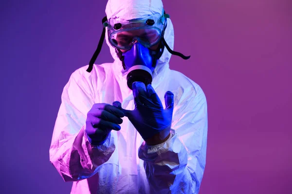 Coronavirus covid-19 pandemic. Doctor scientist wearing protective biological suit and mask due to global healthcare epidemic warning and danger background in blue and pink neon lights background