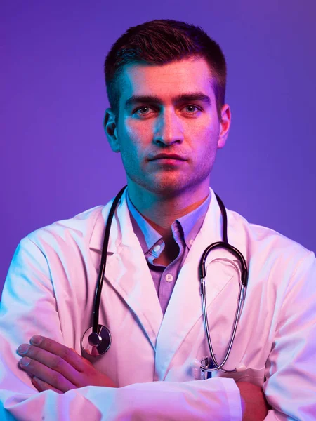白衣英雄的画像 带着听诊器的快乐微笑的年轻医生站在蓝色和粉色的背景下 Coronavirus Covid 19危险警报 高质量的照片 — 图库照片