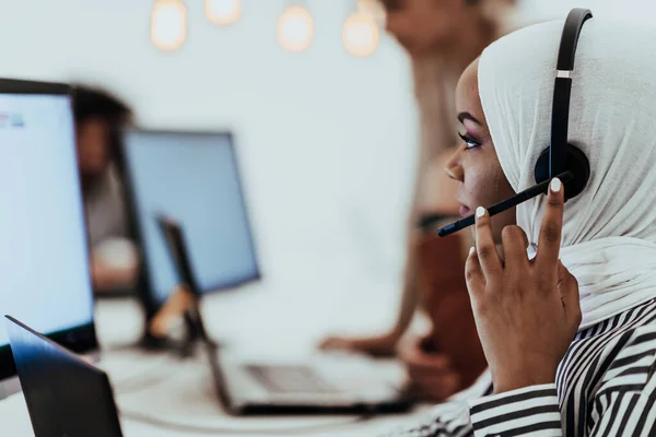 African American Muslim woman with hijab and headset working as customer support in a modern office