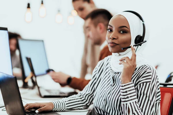 African American Muslim woman with hijab and headset working as customer support in a modern office