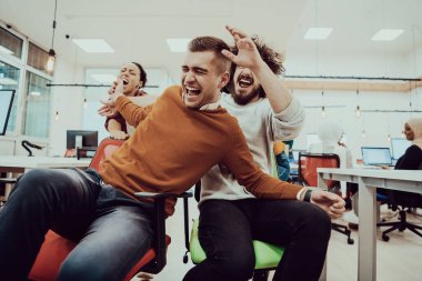 Takım oluşturma ve ofis eğlencesi. Şık giyinen neşeli iş adamları ofis sandalyelerinde yarışırken eğleniyorlar ve gülümsüyorlar.