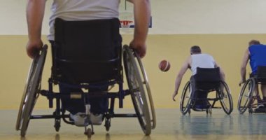 Tekerlekli sandalyede oturan ve spor salonunda basketbol oynayan engelli bir sporcunun yakın çekimi. Seçici odaklanma. Yüksek kalite 4K video. 