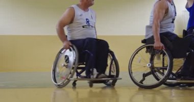 Tekerlekli sandalyede oturan ve spor salonunda basketbol oynayan engelli bir sporcunun yakın çekimi. Seçici odaklanma. Yüksek kalite 4K video. 