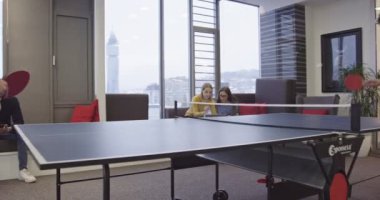 Günlük iş hayatına başlamak. İş adamları modern yaratıcı ofis alanında masa tenisi oynarken bir grup kadın iş arkadaşı proje üzerinde çalışıyor ve arka planda buluşuyorlar. Yüksek kalite