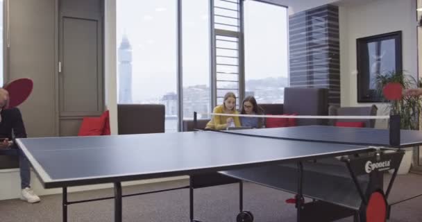 スタートアップビジネスの日常生活 現代のクリエイティブオフィスで卓球をしているビジネスマンと プロジェクトに取り組んでいる女性同僚のグループが集まり 背景にミーティングをしています 高品質 — ストック動画