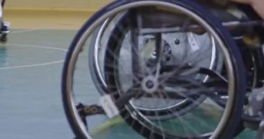 Tekerlekli sandalyede oturan ve spor salonunda basketbol oynayan engelli bir sporcunun yakın çekimi. Seçici odaklanma. Yüksek kalite 4K video. 