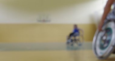 Tekerlekli sandalyede oturan ve spor salonunda basketbol oynayan engelli bir sporcunun yakın çekimi. Seçici odaklanma. Yüksek kalite 4K video. 