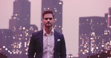 Yakışıklı iş adamı pozu gülümse ve bak kamera gecesi New York Skyline City ofis binaları arka planda. Yüksek kalite 8K görüntü
