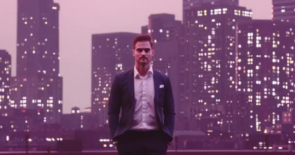 英俊潇洒的商人挂着笑脸 看着相机之夜纽约天际线城楼的背景图 高质量的8K镜头 — 图库视频影像