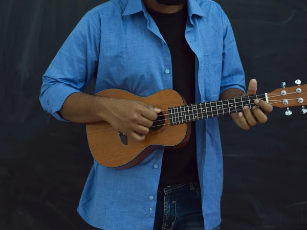身穿蓝色衬衫 戴着眼镜 在学校黑板前弹奏吉他的印度年轻人 — 图库照片