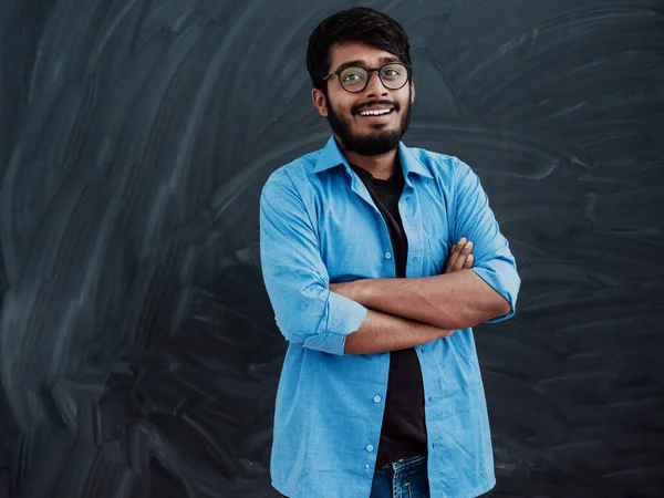 学校の黒板の前で腕を組んでポーズをとる青いシャツを着た若いインド人学生 — ストック写真