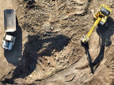 Endüstriyel maden kazıcıları inşaat alanındaki toprağı kazıyor ve kamyonları yüklüyor. Hava aracı üst görüntüsü. Merhaba kaliteli 4K video.