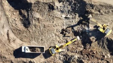 Endüstriyel maden kazıcıları inşaat alanındaki toprağı kazıyor ve kamyonları yüklüyor. Hava aracı üst görüntüsü. Merhaba kaliteli 4K video.