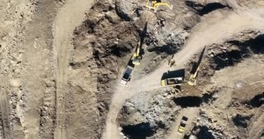 Endüstriyel maden kazıcıları inşaat alanındaki toprağı kazıyor ve kamyonları yüklüyor. Hava aracı üst görüntüsü. Merhaba kaliteli 4K video.