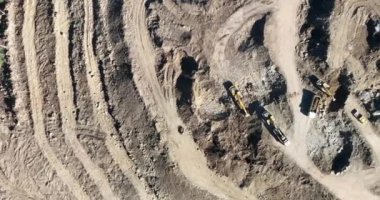 Endüstriyel maden kazıcıları inşaat alanındaki toprağı kazıyor ve kamyonları yüklüyor. Hava aracı üst görüntüsü. Merhaba kaliteli 4K video.