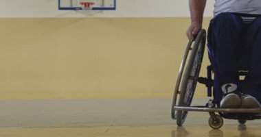 Tekerlekli sandalyede oturan ve spor salonunda basketbol oynayan engelli bir sporcunun yakın çekimi. Seçici odaklanma. Yüksek kalite 4K video. 