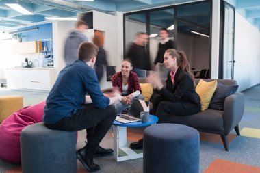 Çok ırklı bir girişim ekibi modern, açık alan çalışma ofisinde toplanıyor. Beyin fırtınası, dizüstü bilgisayarda çalışmak. Hareket bulanıklığı içinde dolaşan bir grup iş arkadaşı