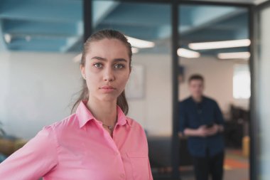 Gencecik gülümseyen iş kadınının portresi. Yaratıcı açık mekan ortak çalışma ofisinde. Başarı sahibi iş kadını, kopyalama alanı ile ofiste duruyor. Arka planda çalışan iş arkadaşları