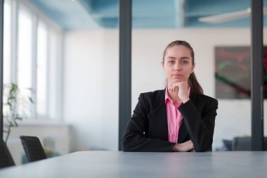Pembe gömlekli başarılı bir bayan lider kararlı bir gülümsemeyle modern cam bir ofiste oturuyor. İş anlayışı ve modern online işlerdeki gençlerin başarısı. 