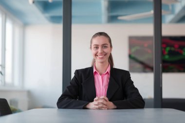 Pembe gömlekli başarılı bir bayan lider kararlı bir gülümsemeyle modern cam bir ofiste oturuyor. İş anlayışı ve modern online işlerdeki gençlerin başarısı. 