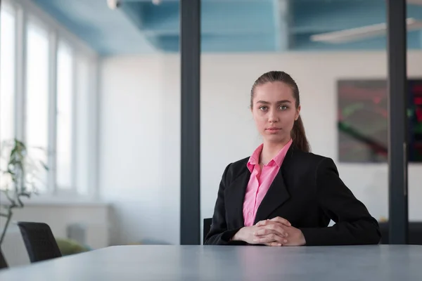 成功的年轻女性领导者 身穿一件粉色衬衫 坐在现代玻璃办公室里 脸上带着坚定的微笑 — 图库照片
