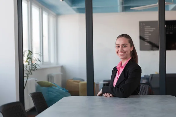 Successful young female leader in a suit with a pink shirt sitting in a modern glass office with a determined smile.Concept of business and the success of young people in modern online businesses
