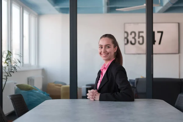 Successful young female leader in a suit with a pink shirt sitting in a modern glass office with a determined smile.Concept of business and the success of young people in modern online businesses