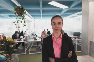 Gencecik gülümseyen iş kadınının portresi. Yaratıcı açık mekan ortak çalışma ofisinde. Başarı sahibi iş kadını, kopyalama alanı ile ofiste duruyor. Arka planda çalışan iş arkadaşları