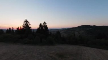 Arka planda güzel bir günbatımı olan güzel çam ağaçları ile tepenin üzerinden hızlı ve manevra yapılabilir bir uçuş. FPV insansız hava aracı ile çekildi. Yüksek kalite 4k görüntü