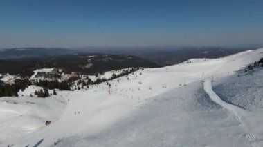 Karlı kışta dağ ve bulutlu bir günde yamaçta kayak yapan insanlar. FPV İHA Jahorina, Bosna-Hersek Olimpiyat Dağı. Yüksek kalite 4K görüntü