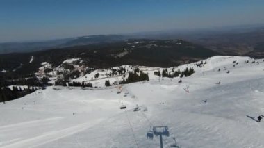 Karlı kışta dağ ve bulutlu bir günde yamaçta kayak yapan insanlar. FPV İHA Jahorina, Bosna-Hersek Olimpiyat Dağı. Yüksek kalite 4K görüntü