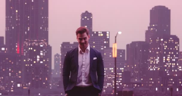 ハンサムなビジネスマンが笑顔をポーズし 背景にカメラナイトニューヨークスカイラインシティオフィスビルを見てください 高画質8K映像 — ストック動画