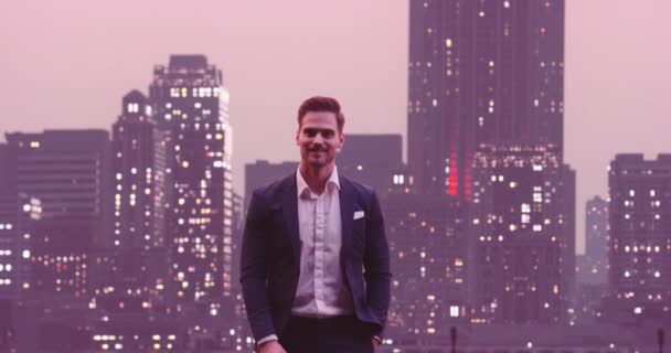 英俊潇洒的商人挂着笑脸 看着相机之夜纽约天际线城楼的背景图 高质量的8K镜头 — 图库视频影像