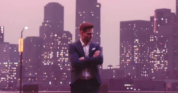 ハンサムなビジネスマンが笑顔をポーズし 背景にカメラナイトニューヨークスカイラインシティオフィスビルを見てください 高画質8K映像 — ストック動画