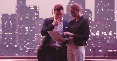 İnsanlar ve teknoloji kavramı. Çekici bir iş çifti olan Arap erkek ve Müslüman kadın şık gündelik tarzda, ofis dışında duruyorlar, dizüstü bilgisayarda birlikte çalışıyorlar, gülümsüyorlar ve tartışıyorlar. Yüksek