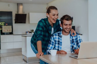 Genç evli bir çift, modern evlerinin oturma odasında otururken bir dizüstü bilgisayarla ebeveynleri, aileleri ve arkadaşlarıyla konuşuyor..