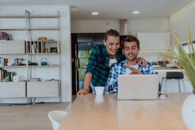 Genç evli bir çift, modern evlerinin oturma odasında otururken bir dizüstü bilgisayarla ebeveynleri, aileleri ve arkadaşlarıyla konuşuyor..