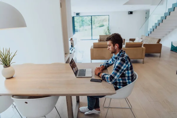 ビジネスビデオチャット 友人やエンターテイメントとの会話のためのラップトップを使用してヘッドフォンで 現代のリビングルームのテーブルに座っている男 — ストック写真