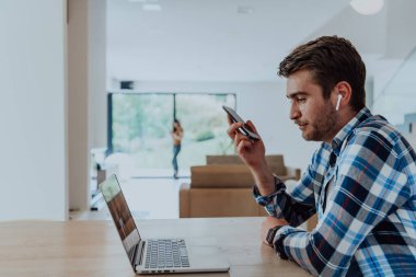 Modern bir oturma odasındaki masada oturan adam akıllı telefon ve dizüstü bilgisayarı iş görüşmesi, arkadaşlarla sohbet ve eğlence için kullanıyor..