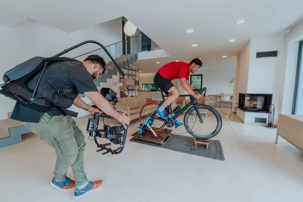 Kamerzysta Filmujący Sportowca Jeżdżącego Rowerze Triatlonowym Symulatorze Nowoczesnym Salonie Szkolenie — Zdjęcie stockowe