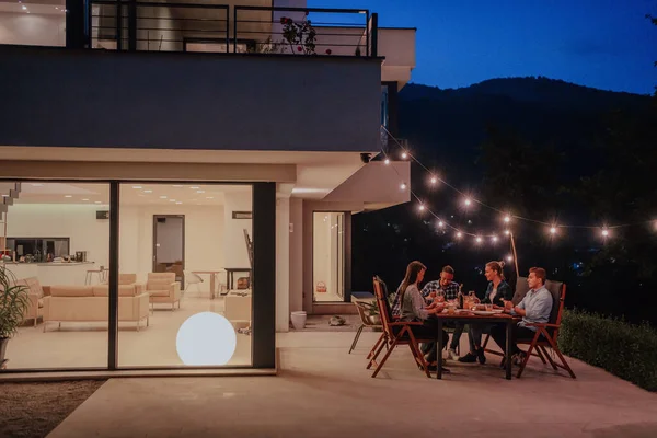 Grupo Jóvenes Diversos Cenando Terraza Una Casa Moderna Por Noche —  Fotos de Stock