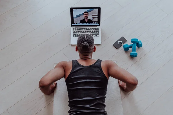 Training At Home. Sporty man doing the training while watching an online tutorial on a laptop, exercising in the living room, free space.