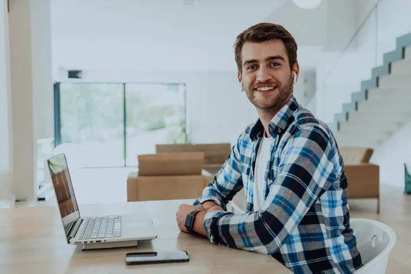 Modern bir oturma odasındaki masada oturan adam, kulaklıklarıyla iş görüşmesi için dizüstü bilgisayar kullanıyor, arkadaşlarıyla sohbet ediyor ve eğleniyor..