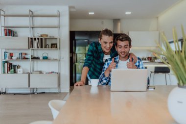 Genç evli bir çift, modern evlerinin oturma odasında otururken bir dizüstü bilgisayarla ebeveynleri, aileleri ve arkadaşlarıyla konuşuyor..