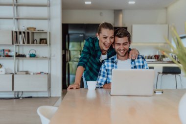 Genç evli bir çift, modern evlerinin oturma odasında otururken bir dizüstü bilgisayarla ebeveynleri, aileleri ve arkadaşlarıyla konuşuyor..