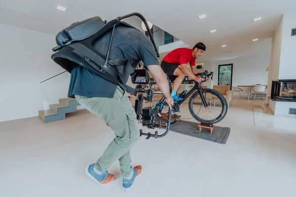 Kamerzysta Filmujący Sportowca Jeżdżącego Rowerze Triatlonowym Symulatorze Nowoczesnym Salonie Szkolenie — Zdjęcie stockowe