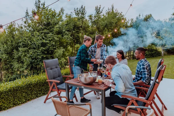 A group of young diverse people having dinner on the terrace of a modern house in the evening. Fun for friends and family. Celebration of holidays, weddings with barbecue